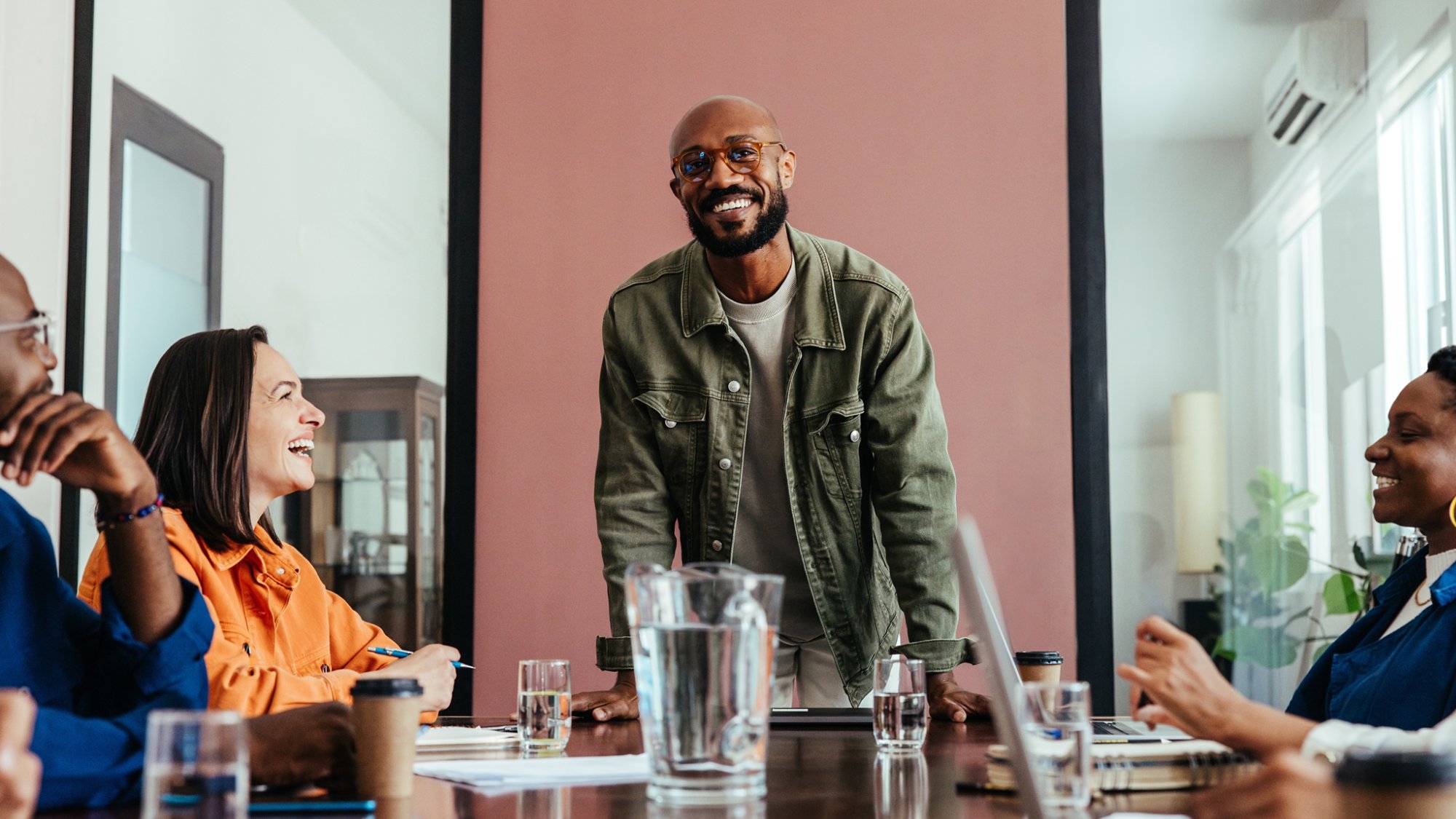 Smiling business leader discussing strategy with a happy team during a meeting in a contemporary boardroom. Team members bonding and collaborating.