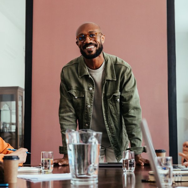 Smiling business leader discussing strategy with a happy team during a meeting in a contemporary boardroom. Team members bonding and collaborating.