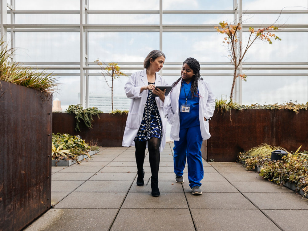 Two doctors walking on a rooftop terrace while looking at an tablet