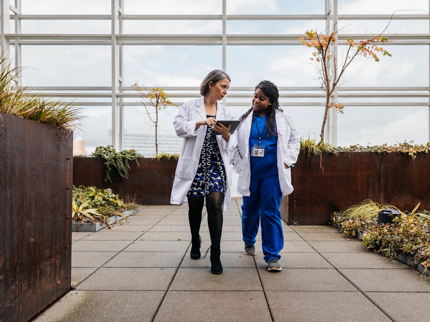 Two doctors walking on a rooftop terrace while looking at an tablet