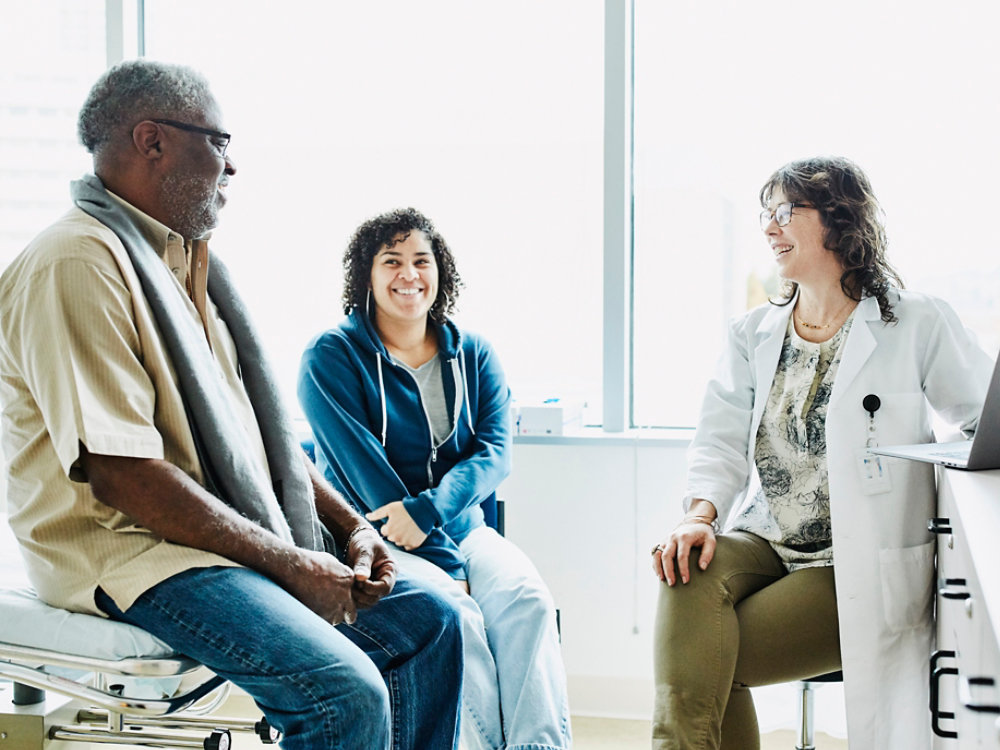 Smiling female doctor consulting with senior male patient and adult daughter in exam room