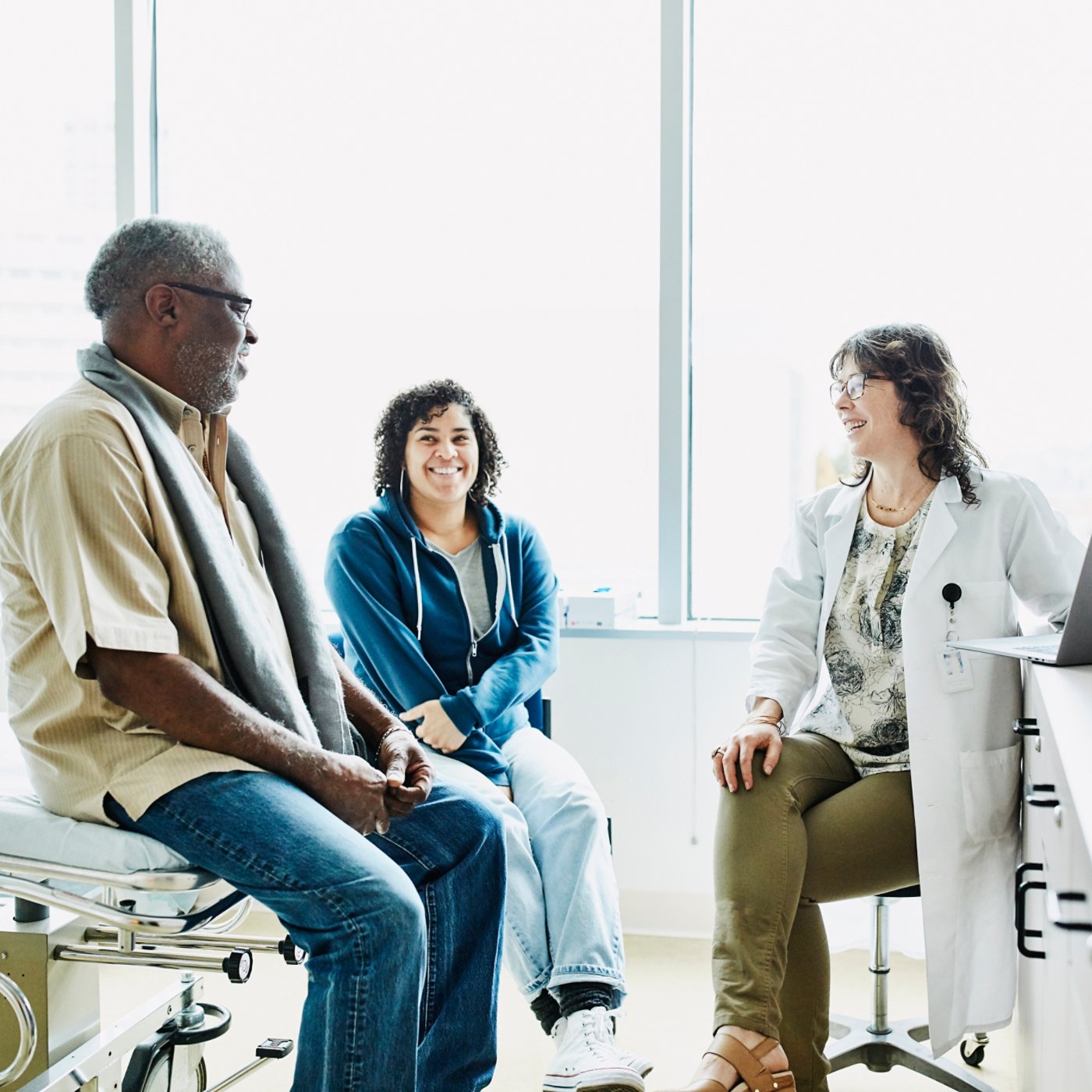 Smiling female doctor consulting with senior male patient and adult daughter in exam room