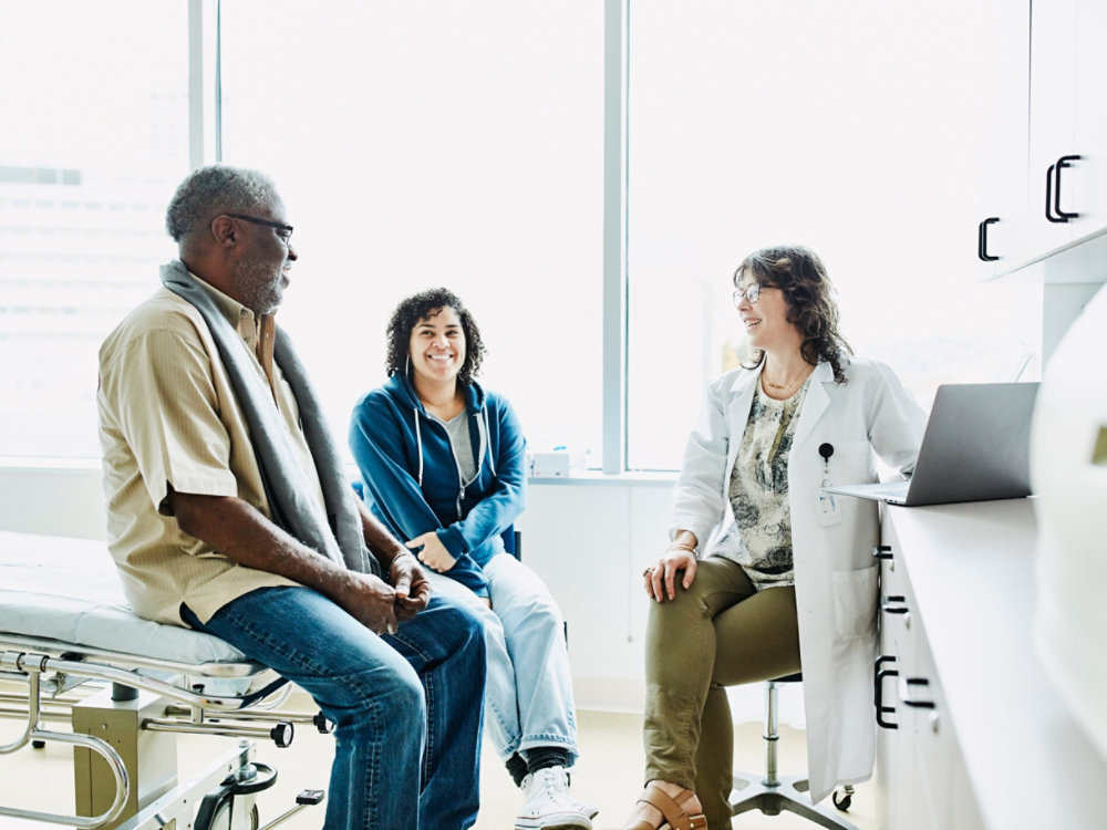 Smiling female doctor consulting with senior male patient and adult daughter in exam room