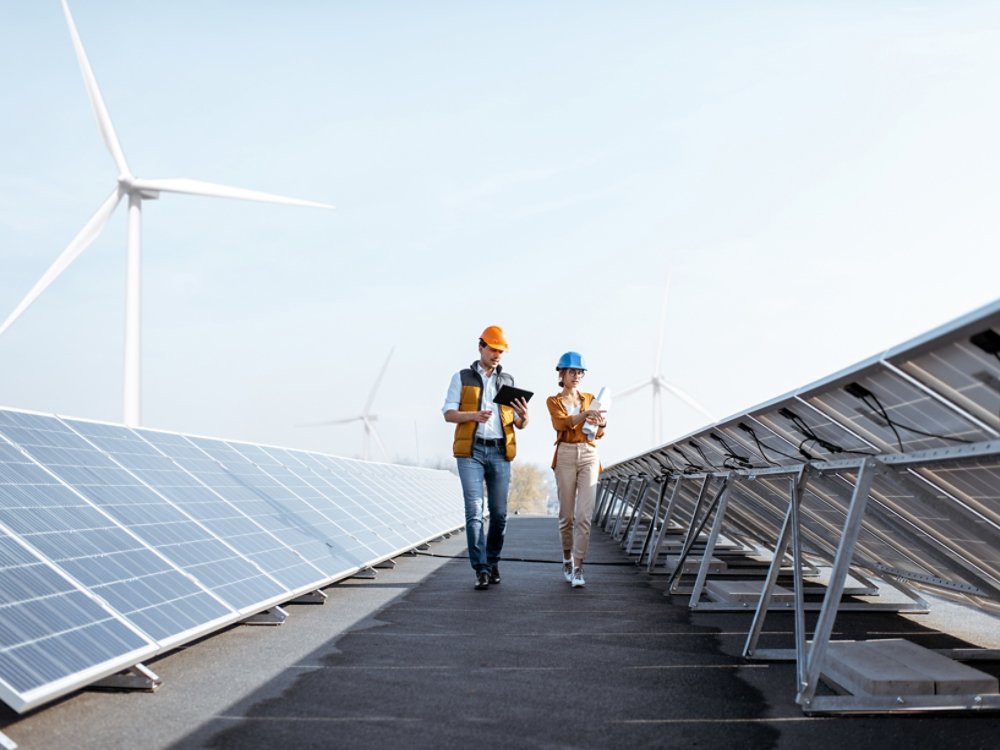 View on the rooftop solar power plant with two engineers walking and examining photovoltaic panels. Concept of alternative energy and its service