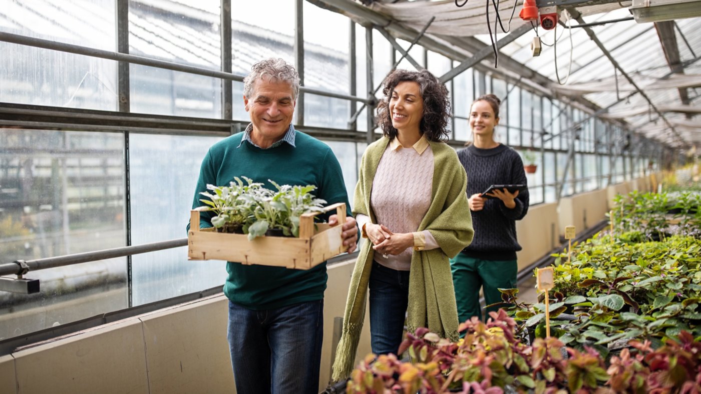 Senior couple buying plants in the garden center with female salesperson at the back. Customer purchasing plants from garden center.