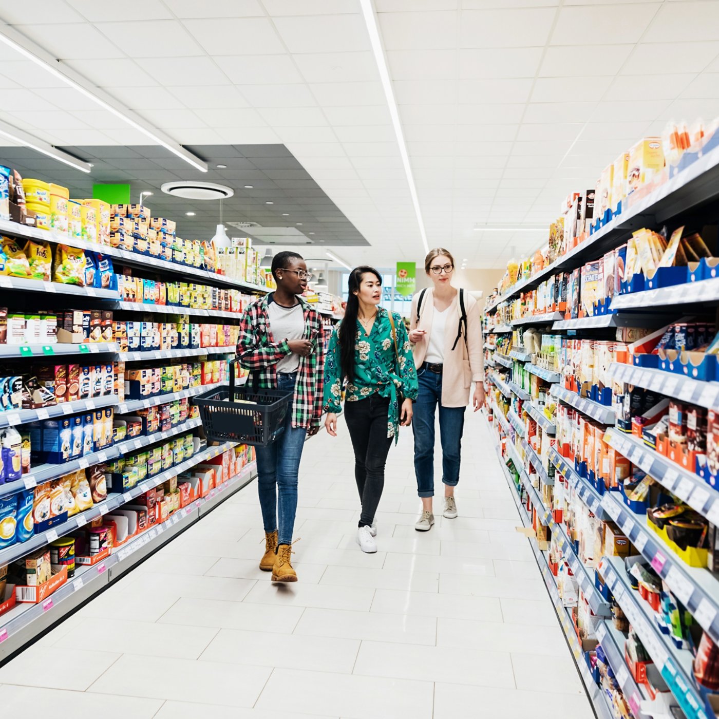 Three girls walking down an isle in the supermarket while out together shopping for food.