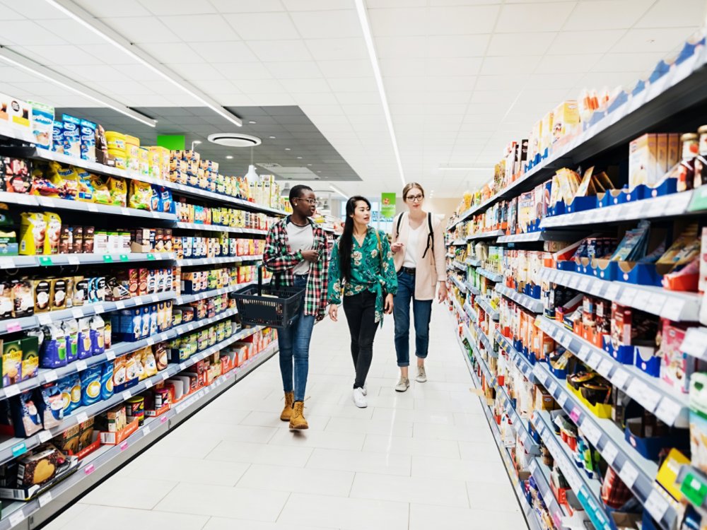 Three girls walking down an isle in the supermarket while out together shopping for food.