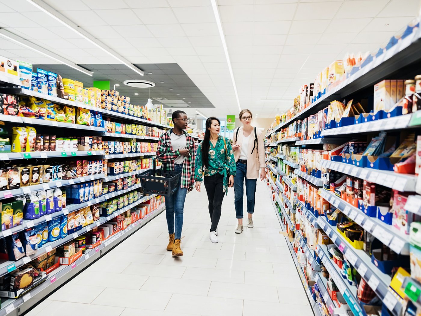 Three girls walking down an isle in the supermarket while out together shopping for food.