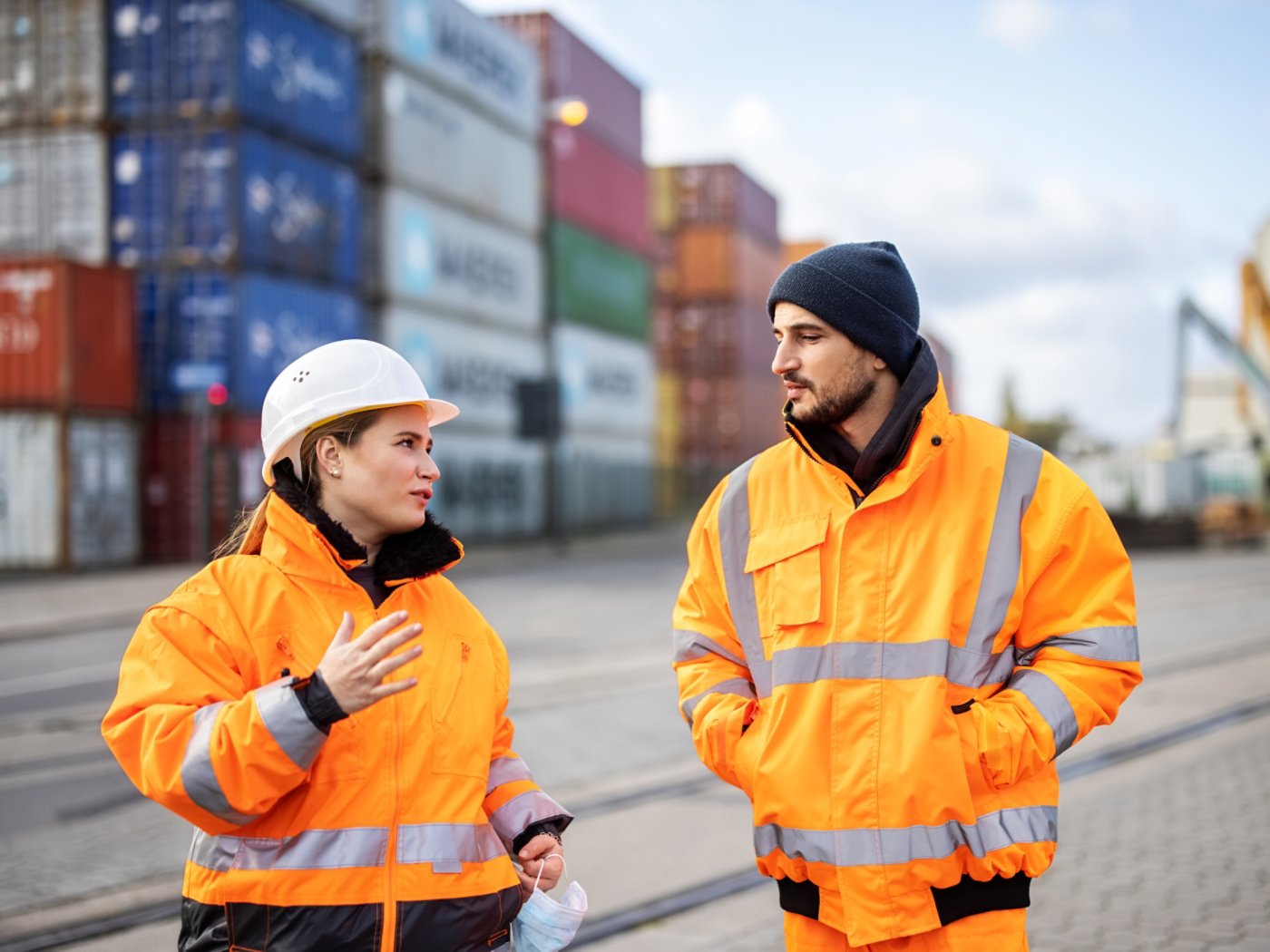 Female engineer talking with a worker at a large commercial dock. Two workers discussing work at the container yard shipping area.