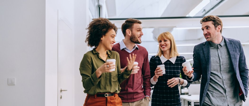 Group of diverse coworkers walking through a corridor in an office, holding paper cups