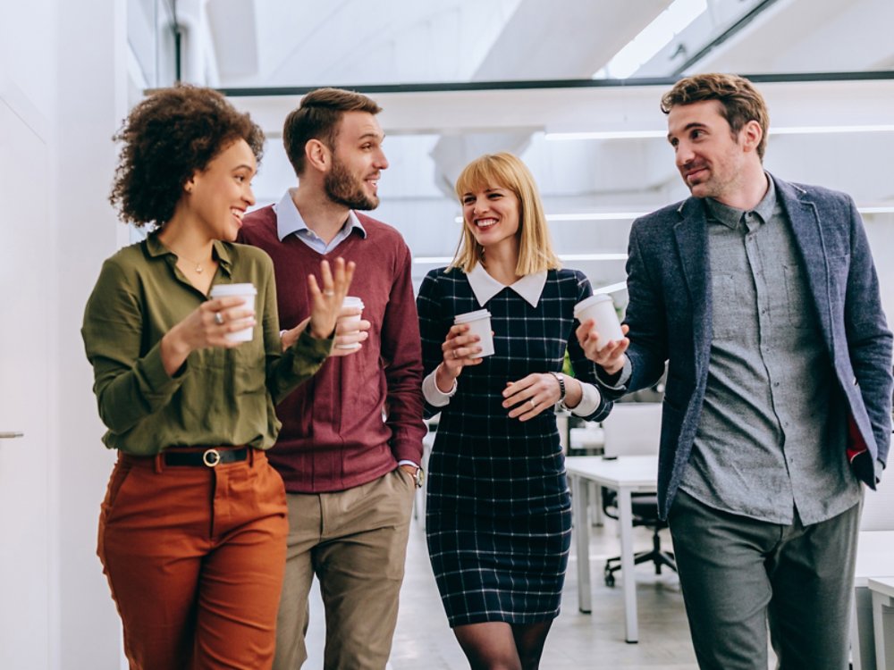 Group of diverse coworkers walking through a corridor in an office, holding paper cups