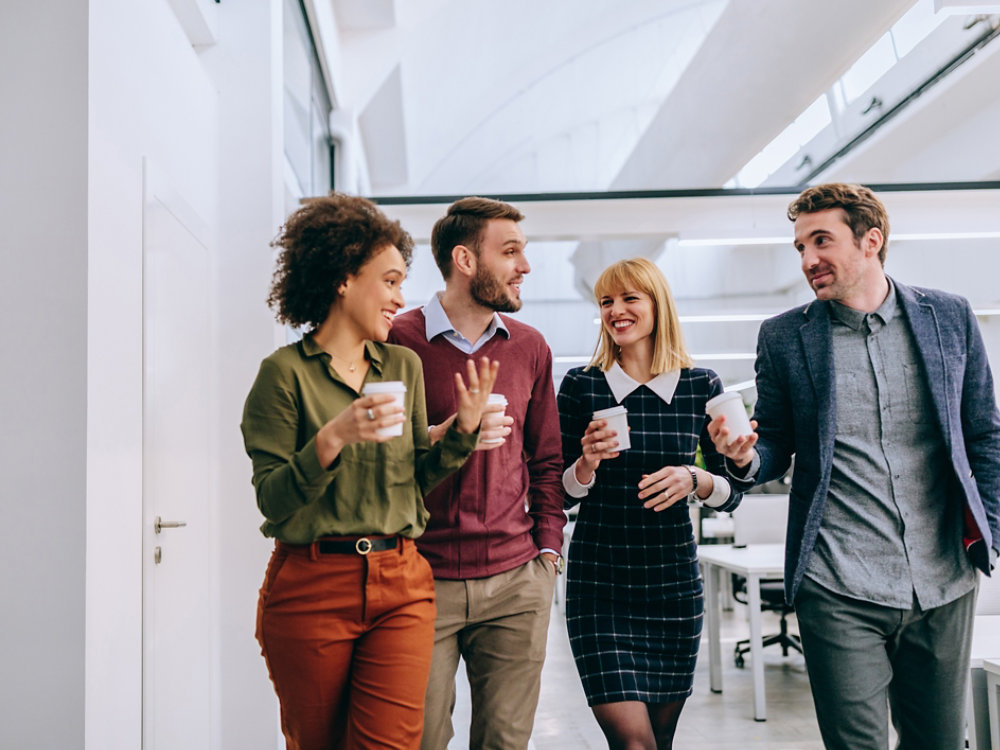 Group of diverse coworkers walking through a corridor in an office, holding paper cups