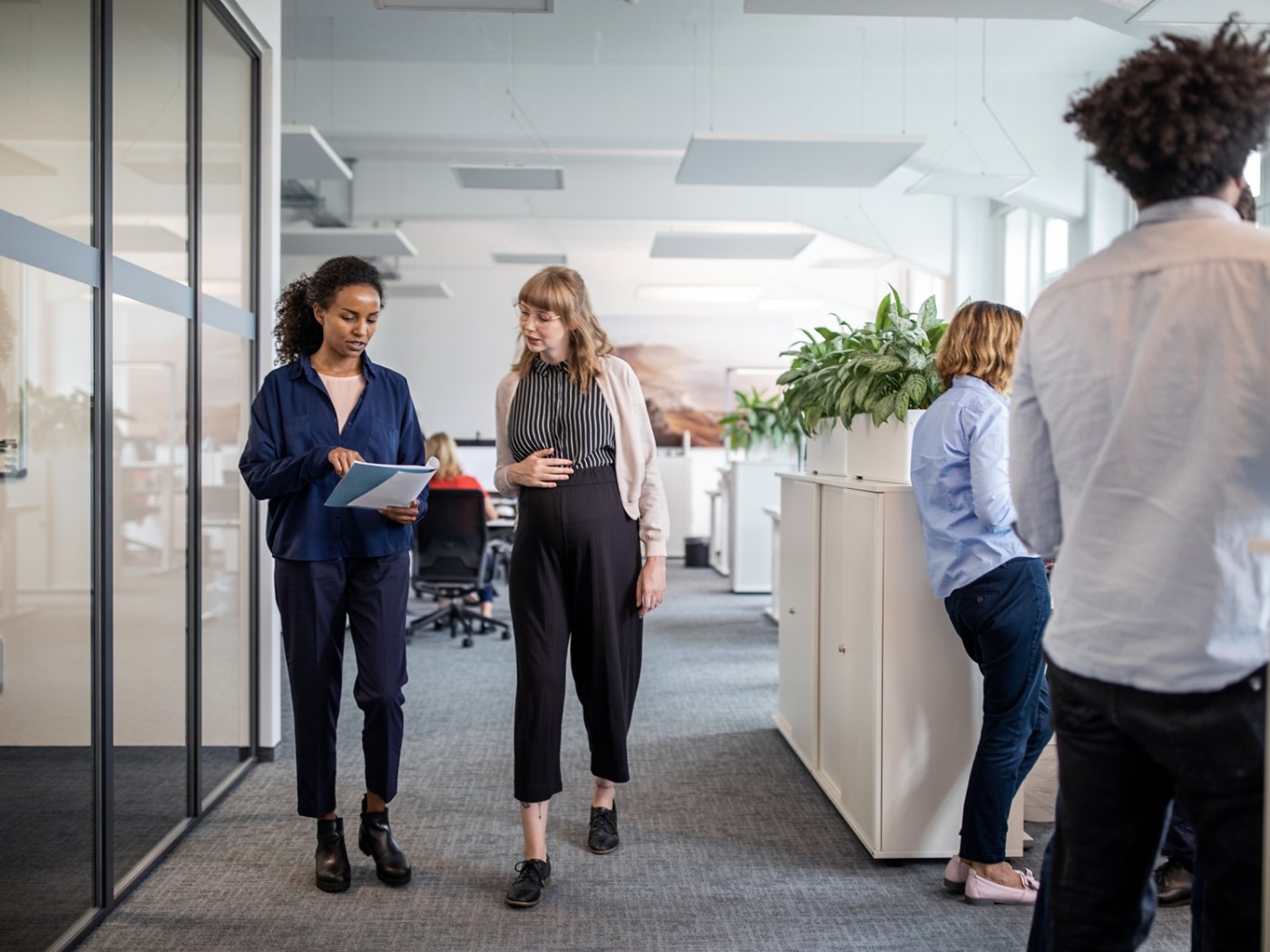 Businesswoman discussing with pregnant colleague over document while walking in creative office