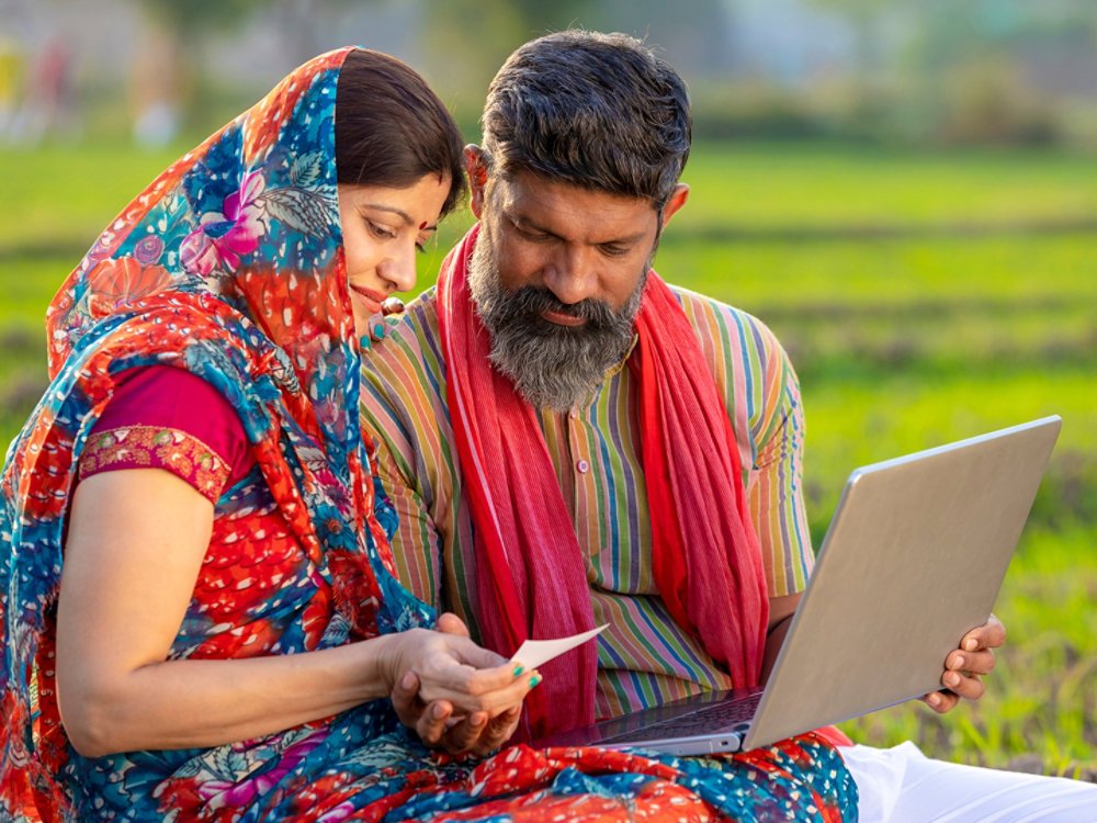 Indian farmer with wife using laptop and bank card at agriculture field.