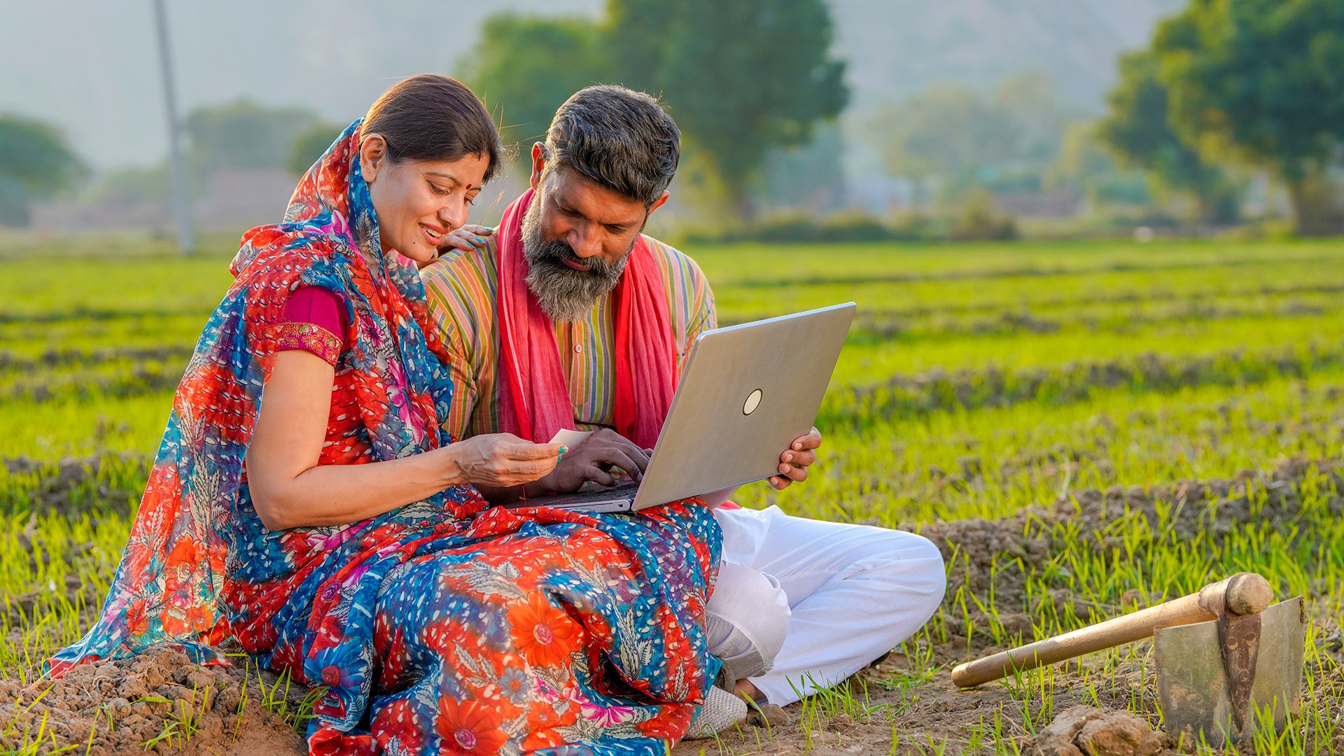 Indian farmer couple use laptop and bank card at agriculture field.