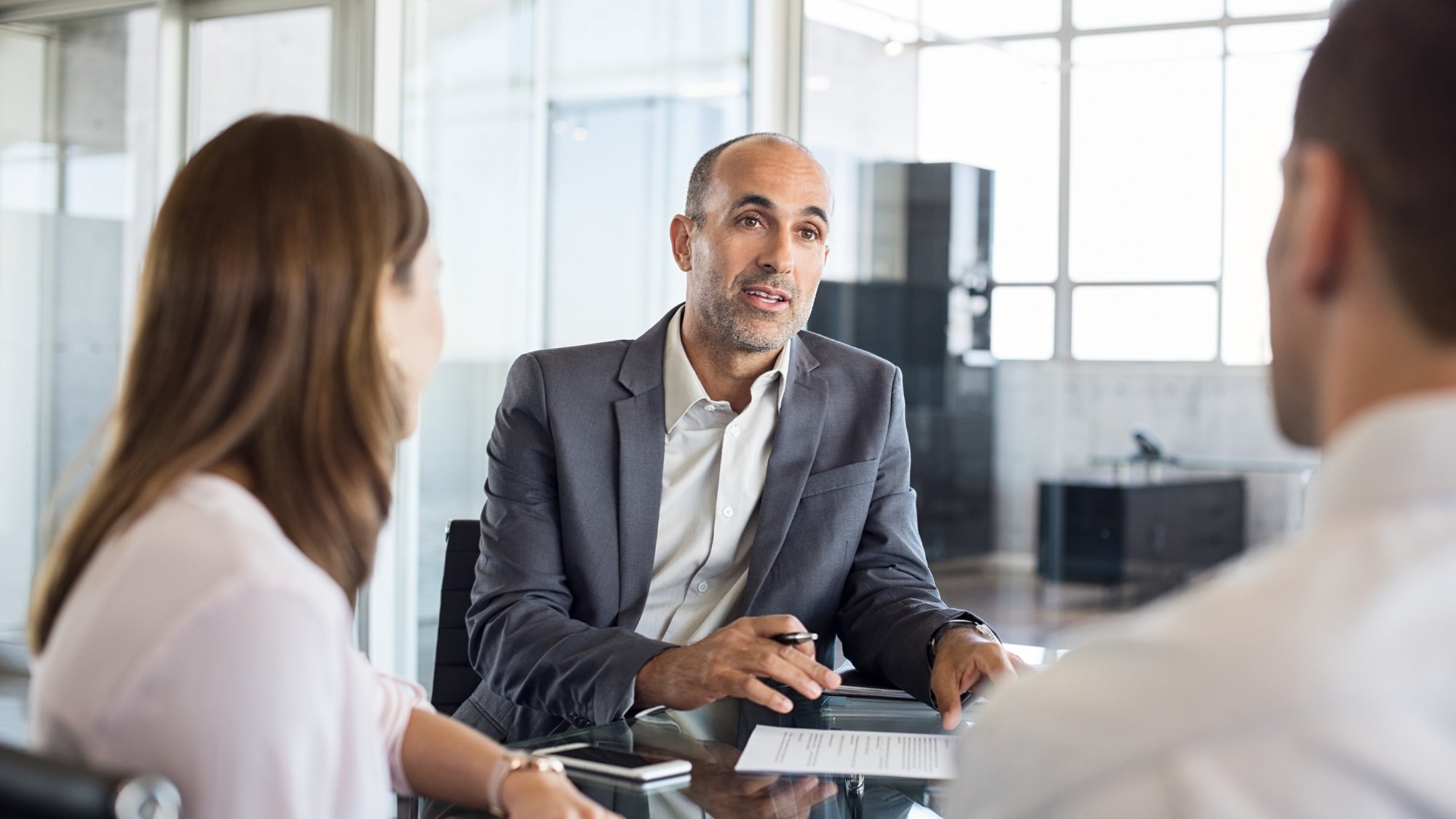 Mature financial agent showing new investment to young couple. Happy financial advisor discussing with a couple their mortgage loan. Happy couple consulting their bank agent about savings plan.