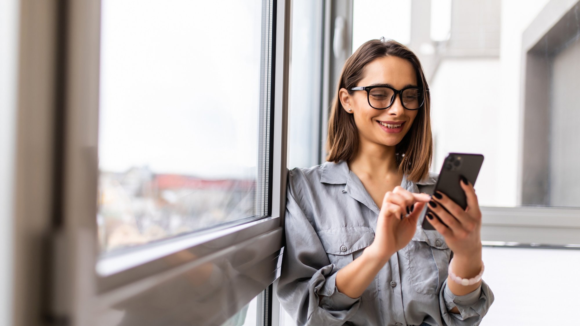 Side view portrait of a casual girl using a smart phone with a warm light near a window of the living room at home