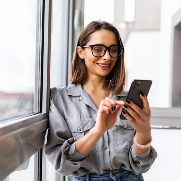 Side view portrait of a casual girl using a smart phone with a warm light near a window of the living room at home