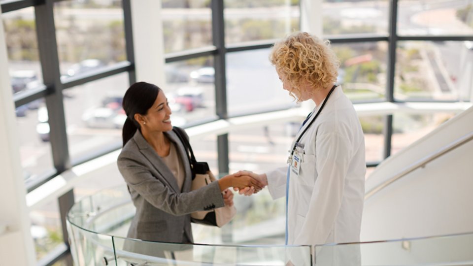 Doctor and businesswoman handshaking on stairs in hospital