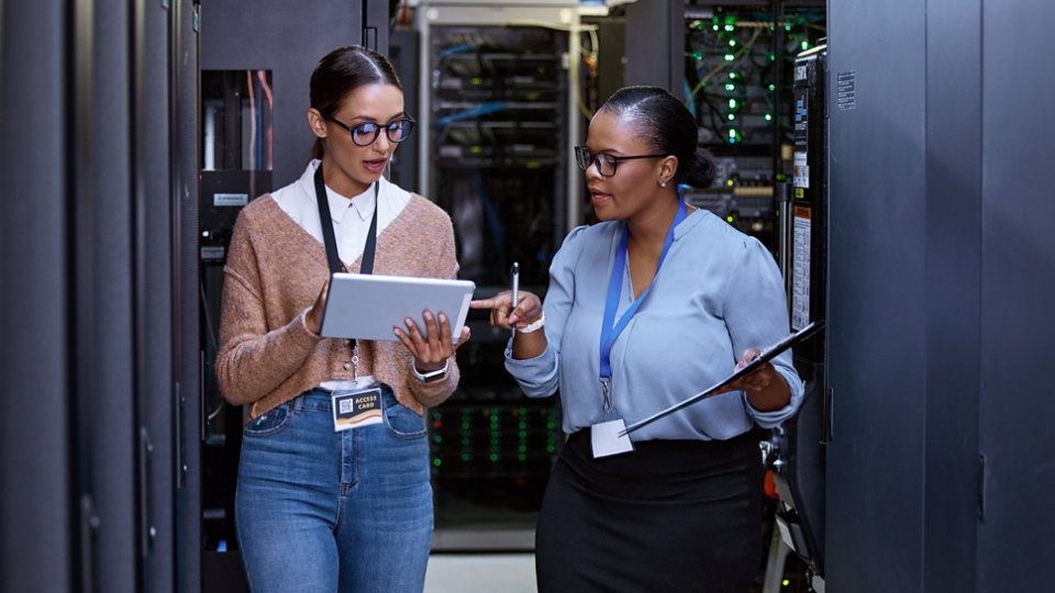 Talking, server room and women with a tablet for cyber security, database planning and inspection. Teamwork, technician and female programmers speaking with technology for coding, hardware and system.