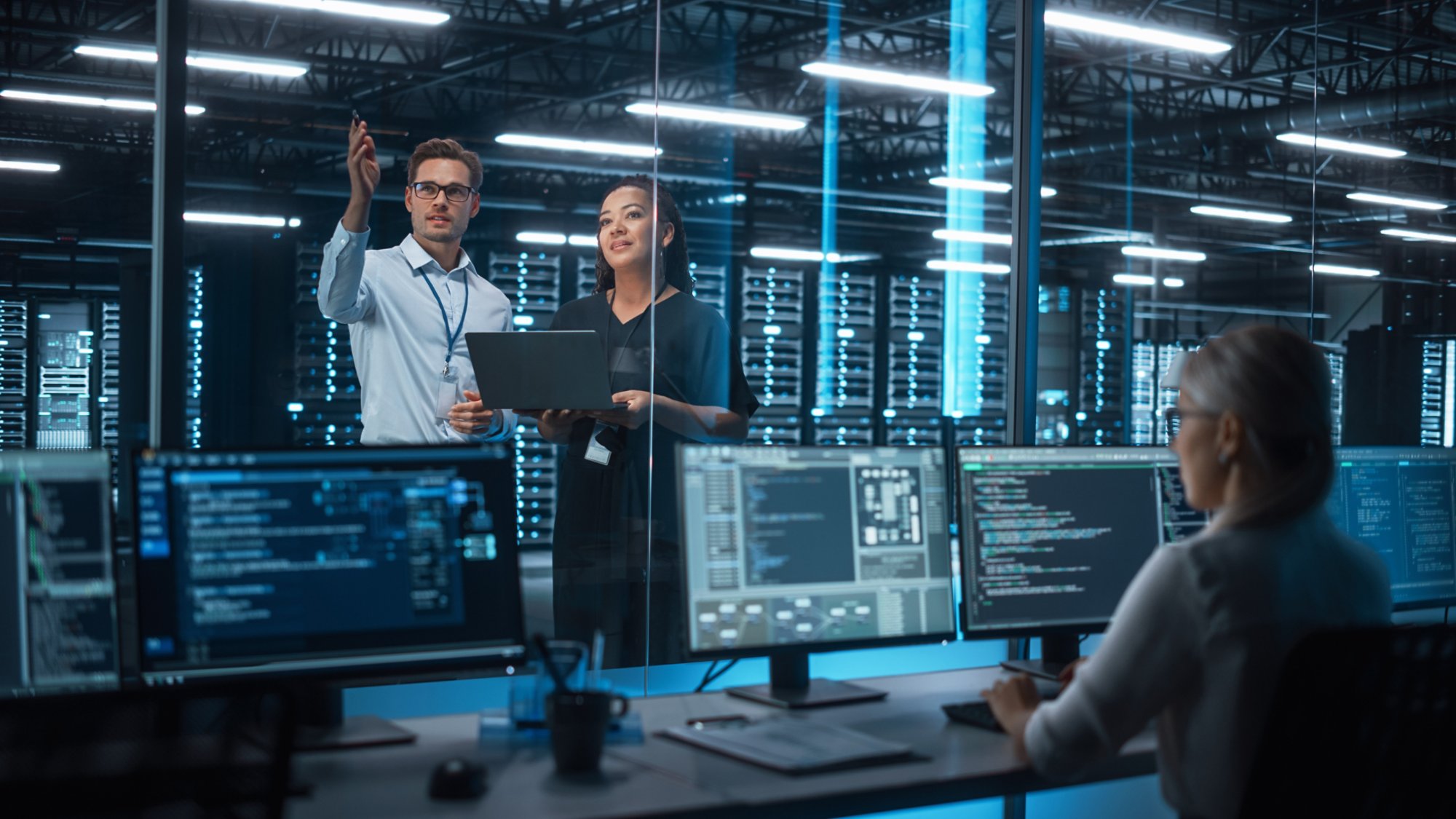 Female e-Business Entrepreneur and Male IT Specialist Discussing Something and Use Laptop in Big Data Center Server Room. Work on Web Services Cloud Computing SAAS Concept