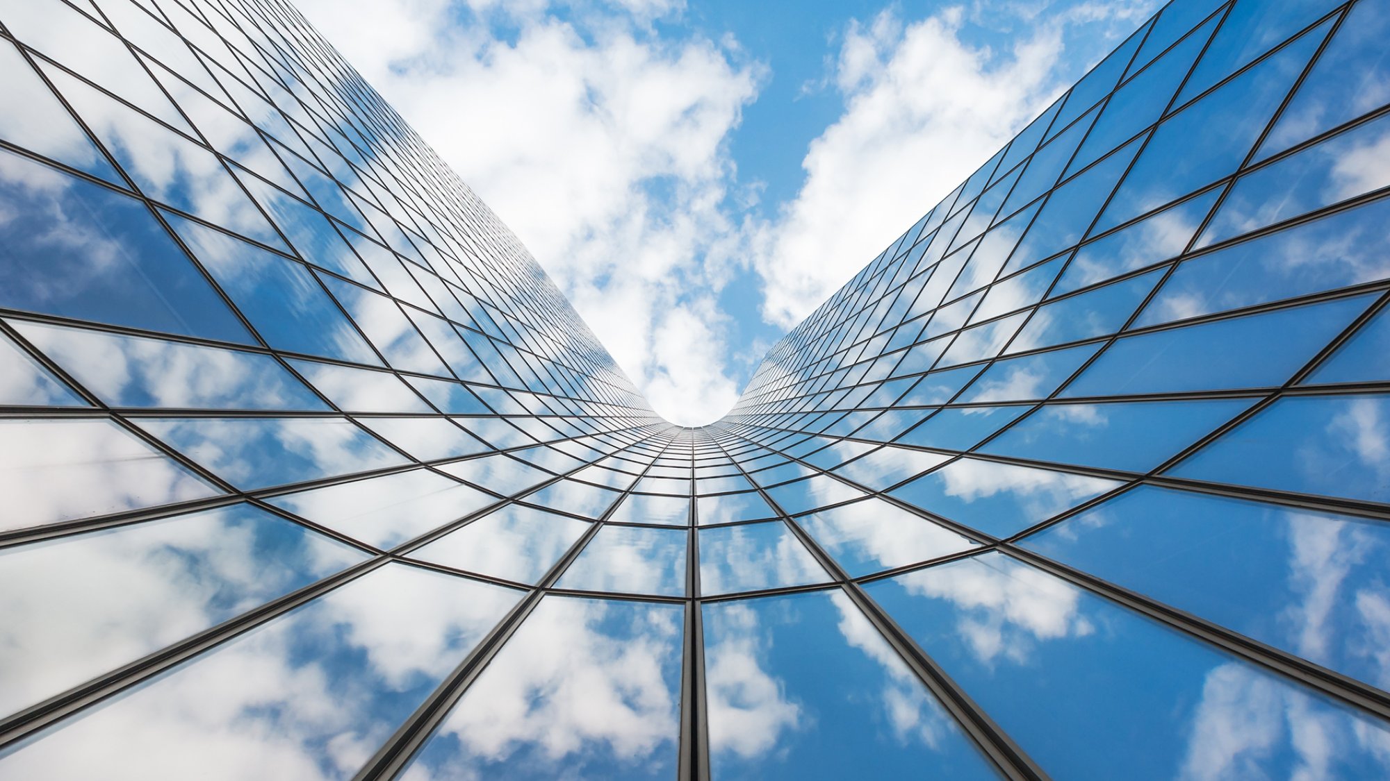 Blue sky and white clouds reflecting in a curved glass building