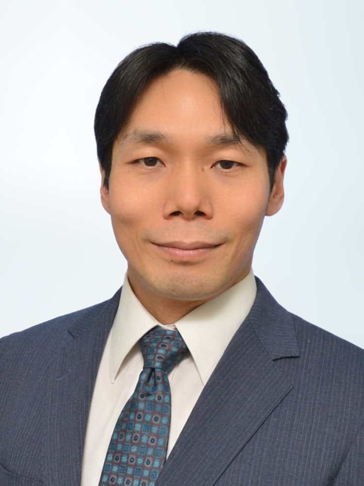 Formal studio portrait of a businessman wearing a dark blue suit, white shirt, and patterned tie. He is facing the camera with a neutral, confident expression. The background is a soft, light gradient that keeps the focus on the subject. The image conveys professionalism and corporate style suitable for business profiles or presentations.