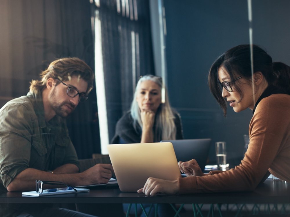 Business woman sharing her ideas with laptop to colleagues. Business people meeting in office and discussing over new project.