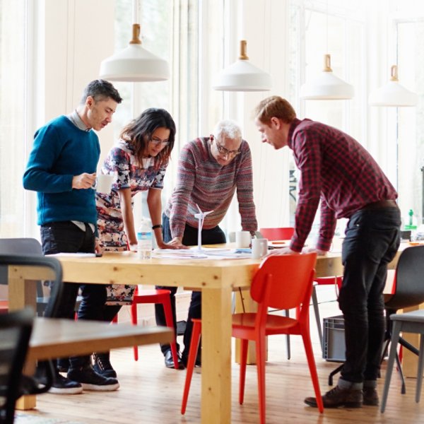 A group of four colleagues standing in an elegant modern office discussing a green energy project