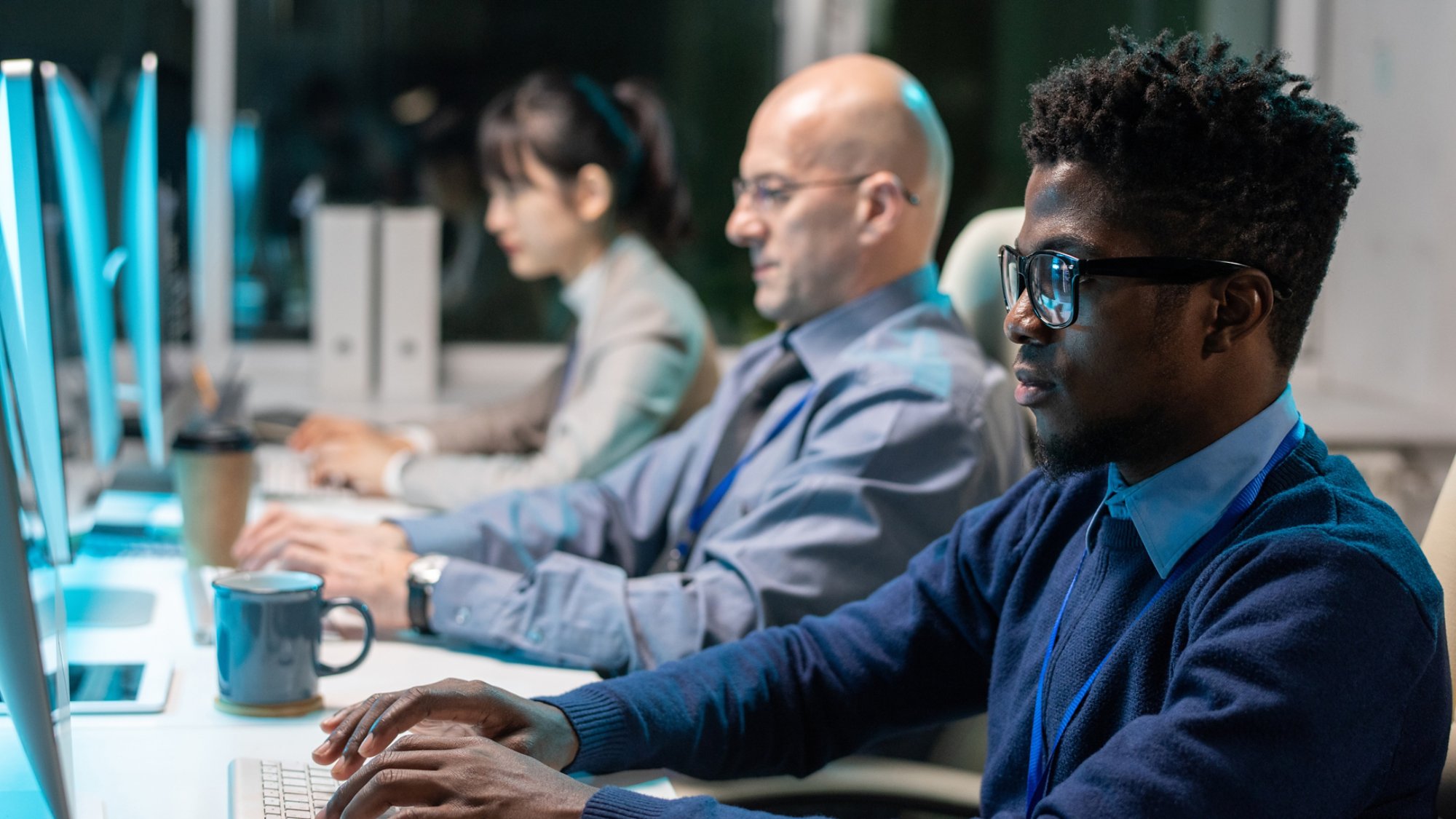 Row of contemporary intercultural programmers working over new software in front of computer monitors in office