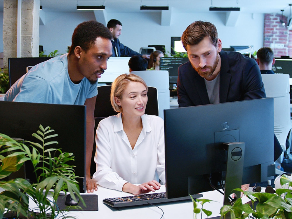 Woman with coworkers discussing working project at computer in coworking space. Multiethic team of developers talking and giving advices. Workday in office. Business concept. Communication. Management