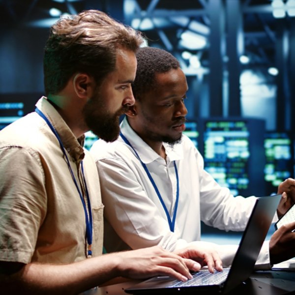 Coworkers running data center hardware diagnostic tests to determine and service software issues. Servicemen using laptop and tablet to fix critical systems, checking for blips