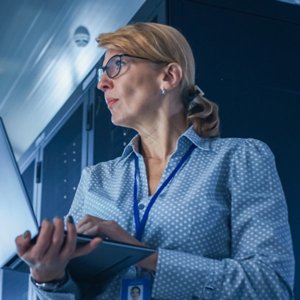 In Data Center: Low-Angle Portrait Shot of a Female IT Technician Running Maintenance Programme on Laptop, Controls Operational Server Rack. Modern High-Tech Telecommunications Operational Data Center