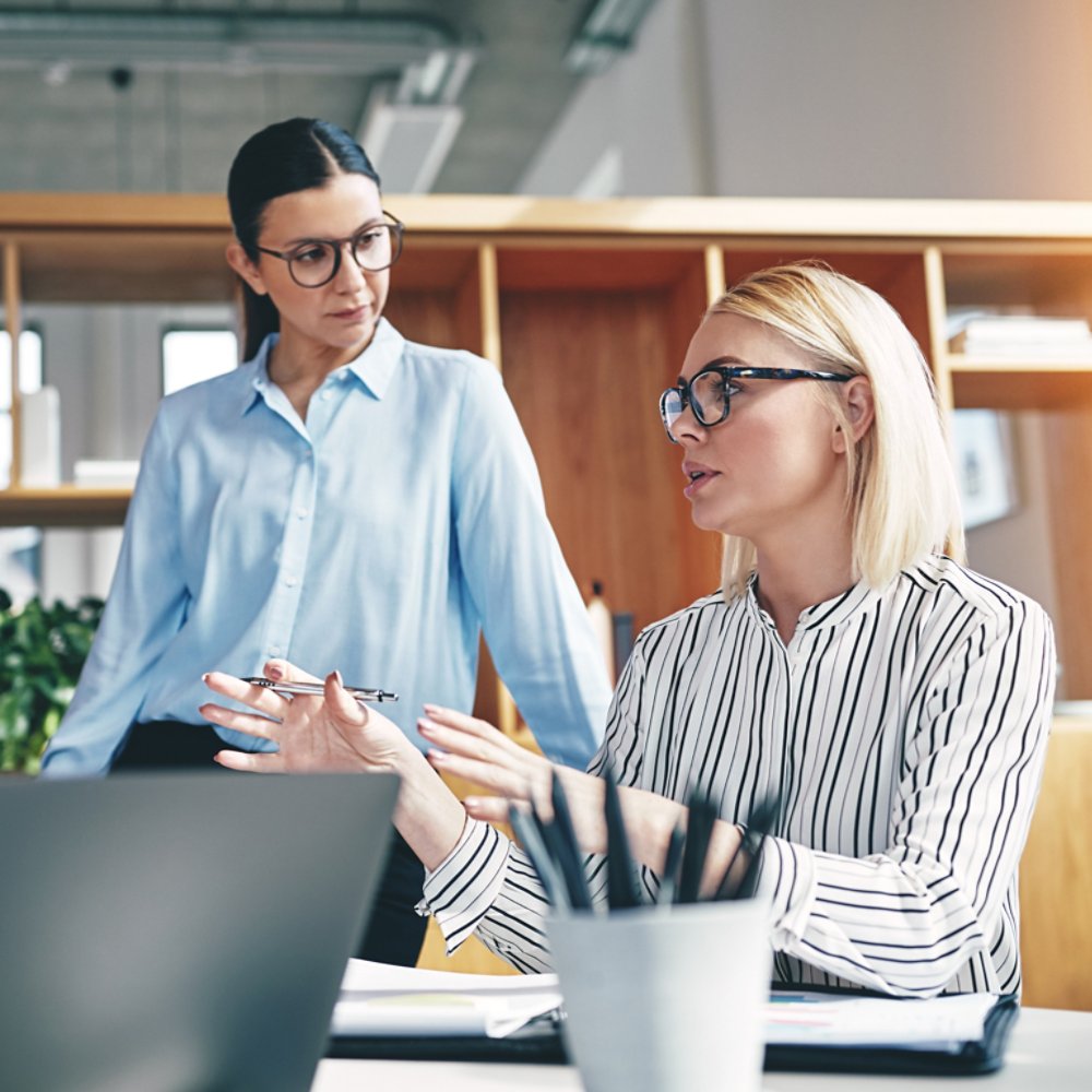Focused young businesswoman explaining an idea with a coworker listening during a meeting together in an office