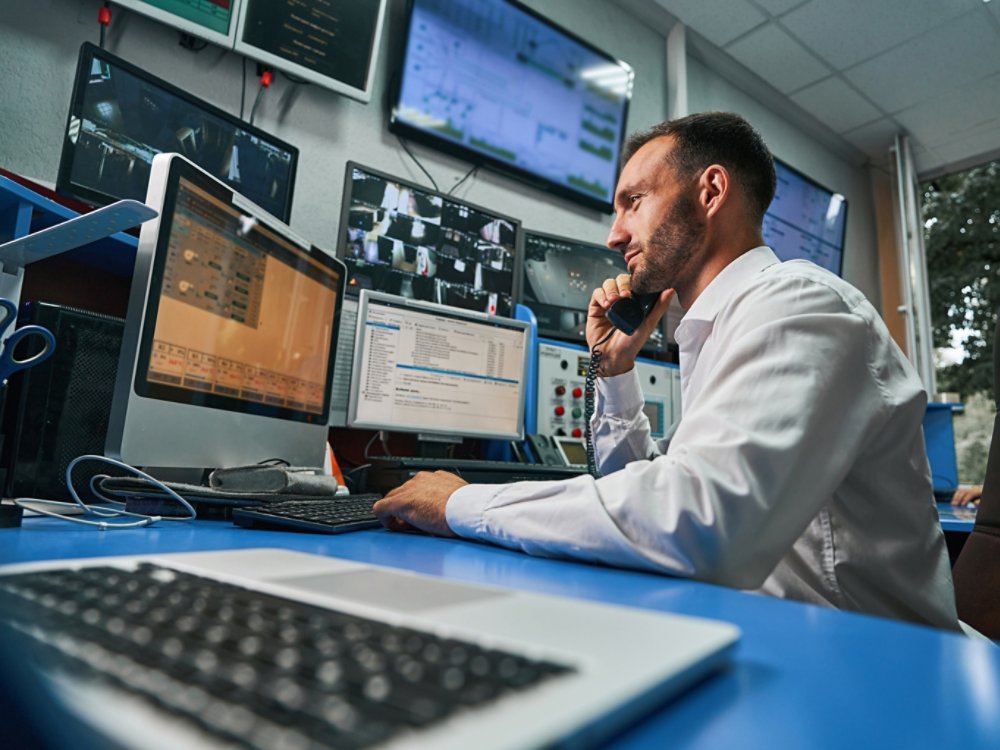Data center operations professional talking on the phone while monitoring network stability through computer
