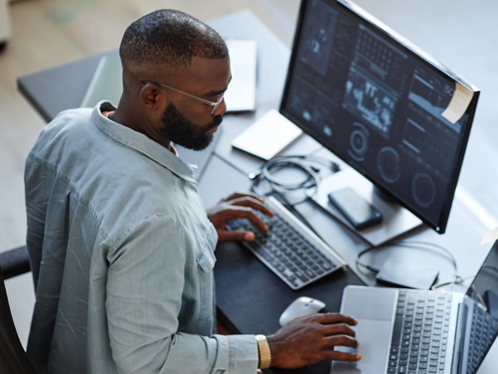 Minimal high angle view at African American software developer working with computers and data systems in office