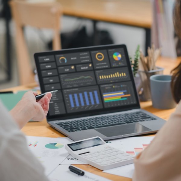 Two businesspeople or an accountant team are analyzing data charts, graphs, and a dashboard on a laptop screen in order to prepare a statistical report and discuss financial data in an office