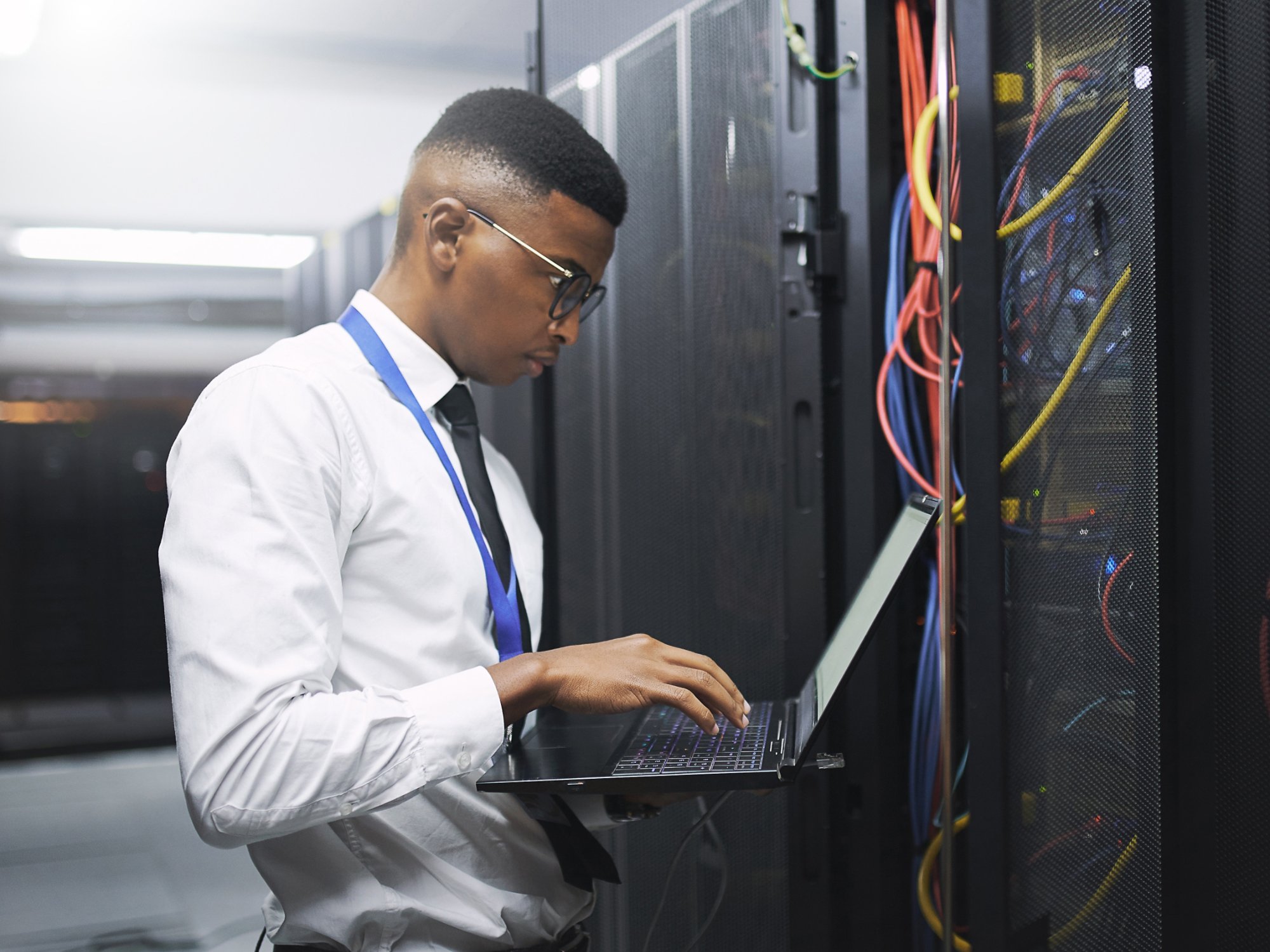 Black man, engineer and server room with laptop for network repair, hardware or storage at data center. Male person, IT technician and computer for technical issue, internet service or system backup.