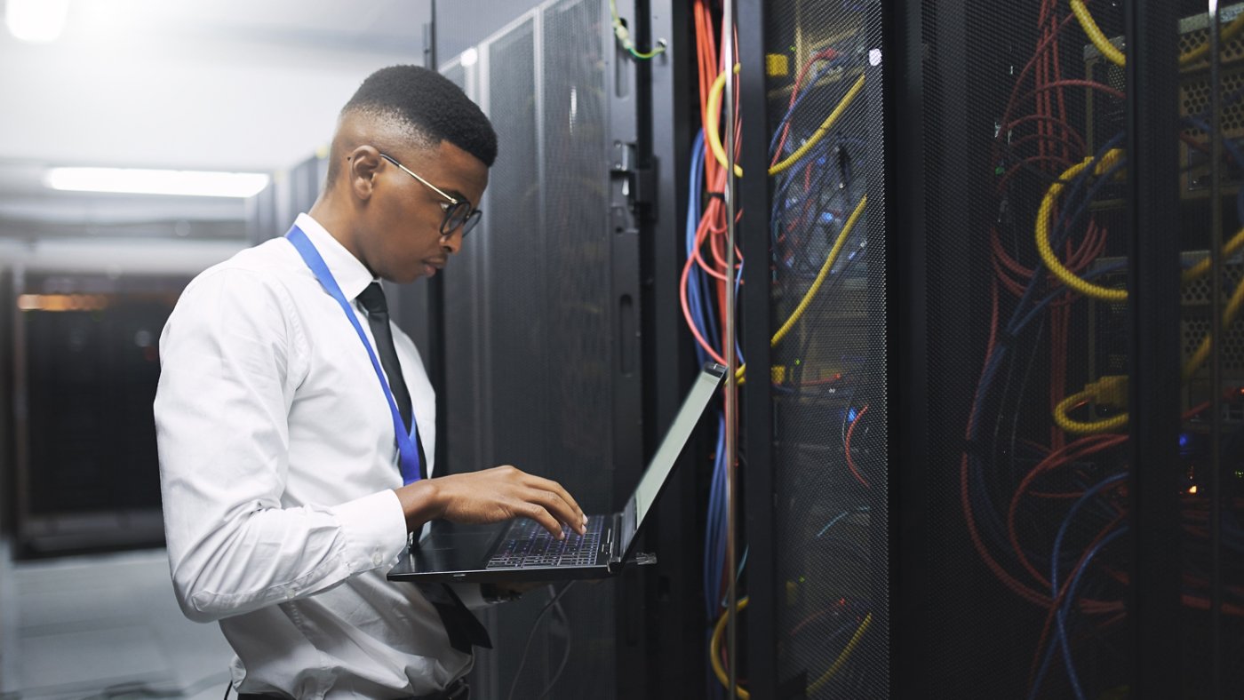 Black man, engineer and server room with laptop for network repair, hardware or storage at data center. Male person, IT technician and computer for technical issue, internet service or system backup.
