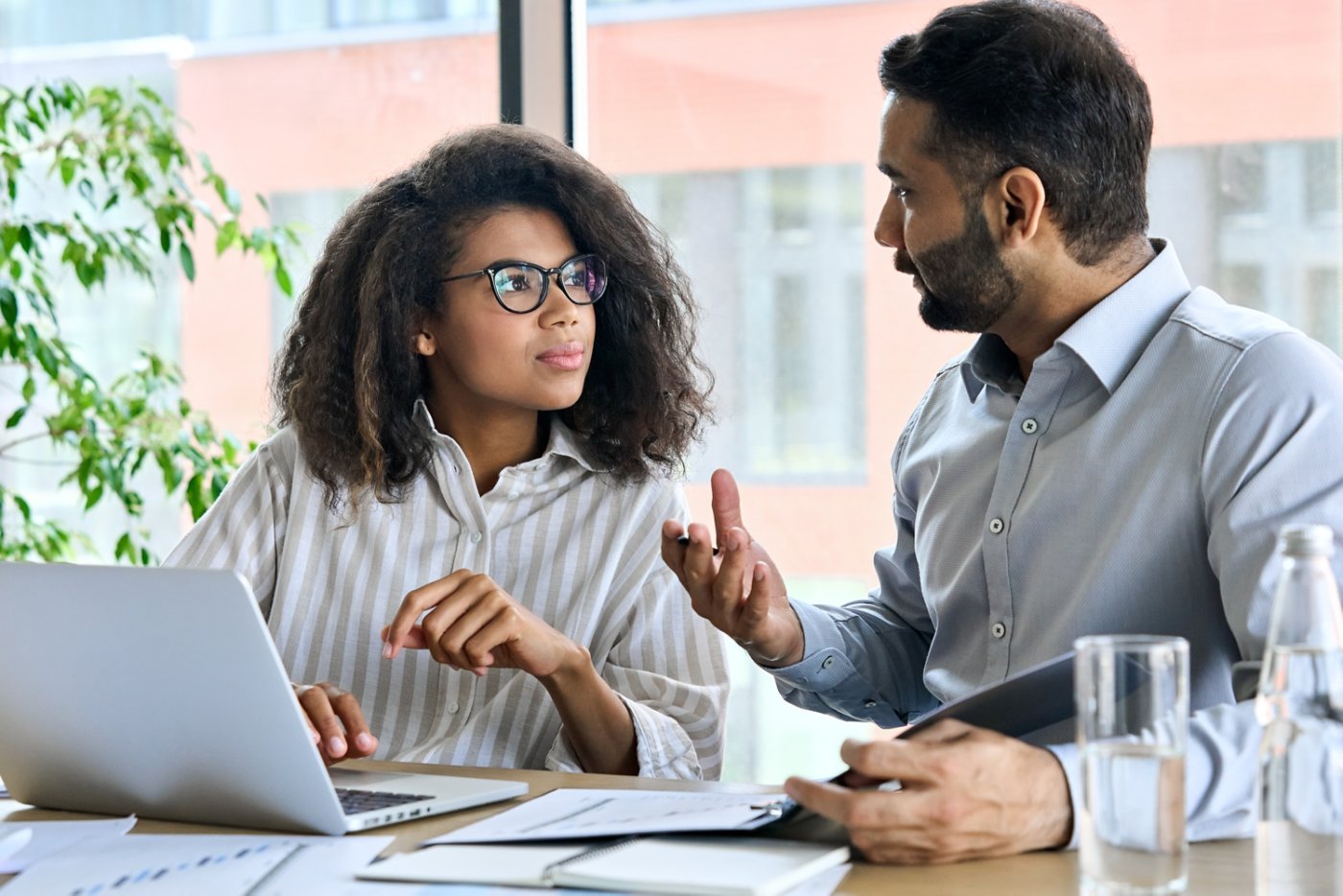 Businessman indian executive manager ceo talking to female African American coworker, using laptop. Diverse multicultural professional partners group discussing business plan at board room meeting.
