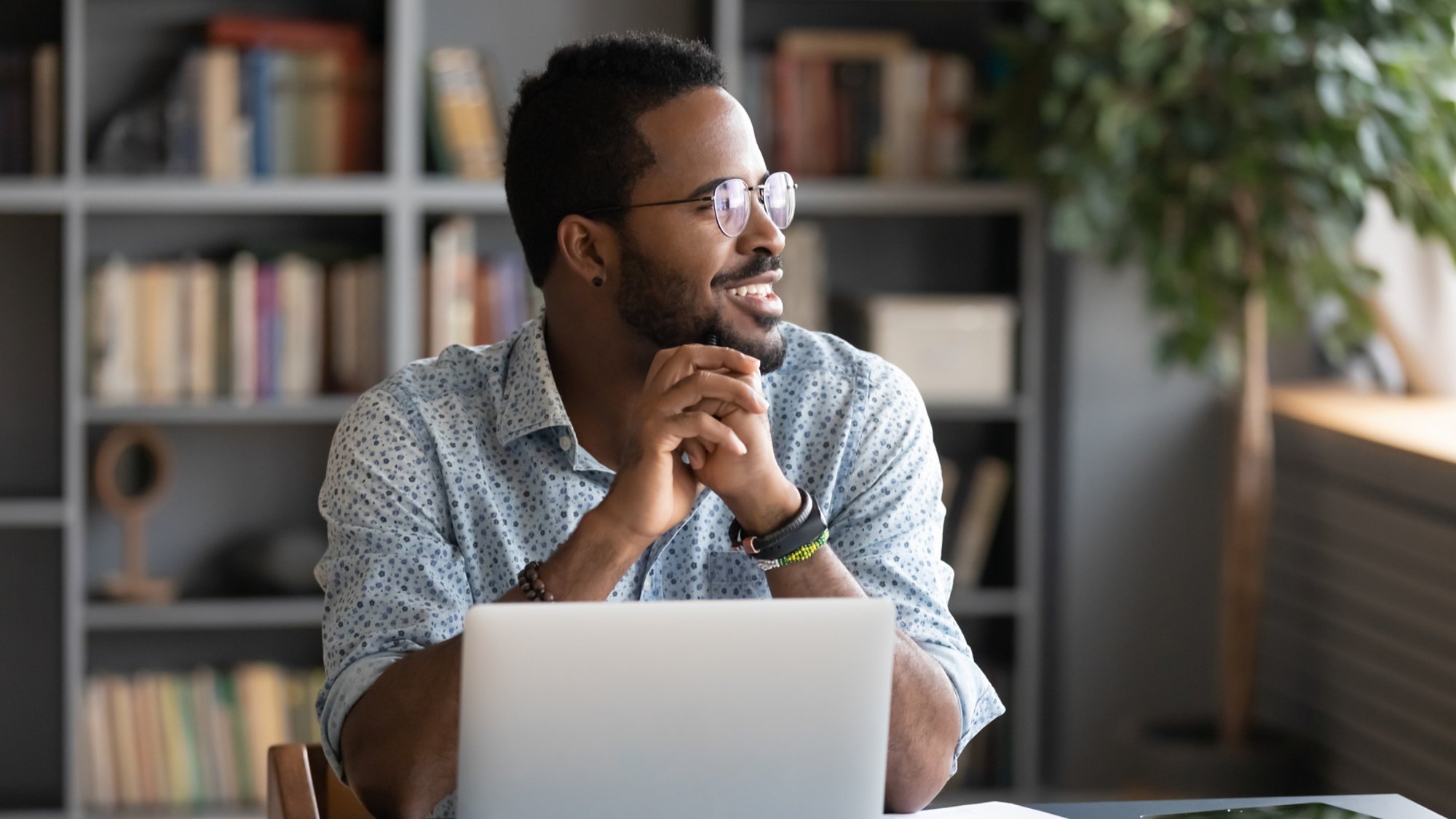 African guy freelancer or office worker take break from work seated at desk in front of laptop looking at window feels satisfied by accomplished work, visualizing relieving fatigue daydreaming concept