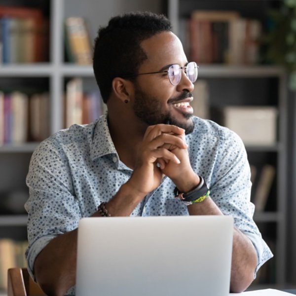 African guy freelancer or office worker take break from work seated at desk in front of laptop looking at window feels satisfied by accomplished work, visualizing relieving fatigue daydreaming concept