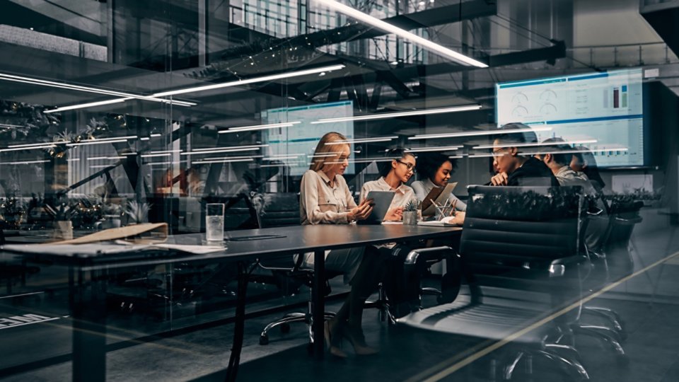 Modern business. Young focused serious business women and men working in a conference room working on a project presentation. Light from a spacious office is reflected through the glass.