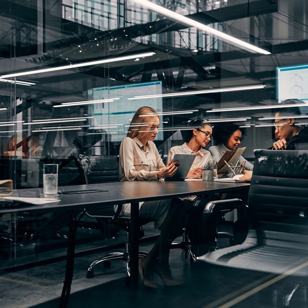 Modern business. Young focused serious business women and men working in a conference room working on a project presentation. Light from a spacious office is reflected through the glass.