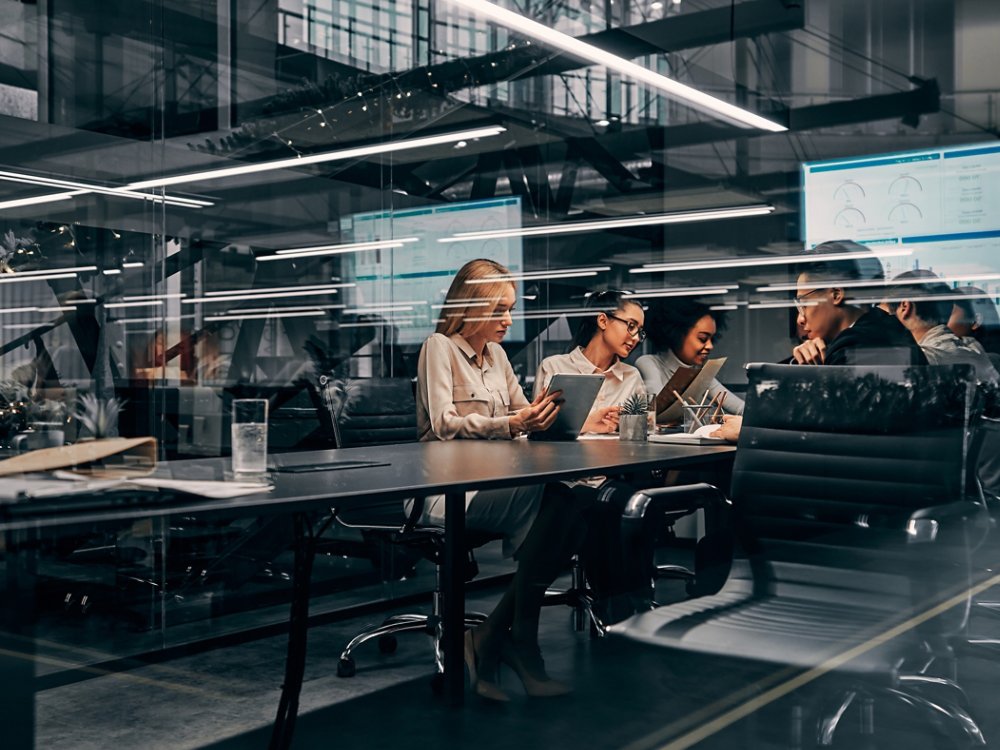 Modern business. Young focused serious business women and men working in a conference room working on a project presentation. Light from a spacious office is reflected through the glass.