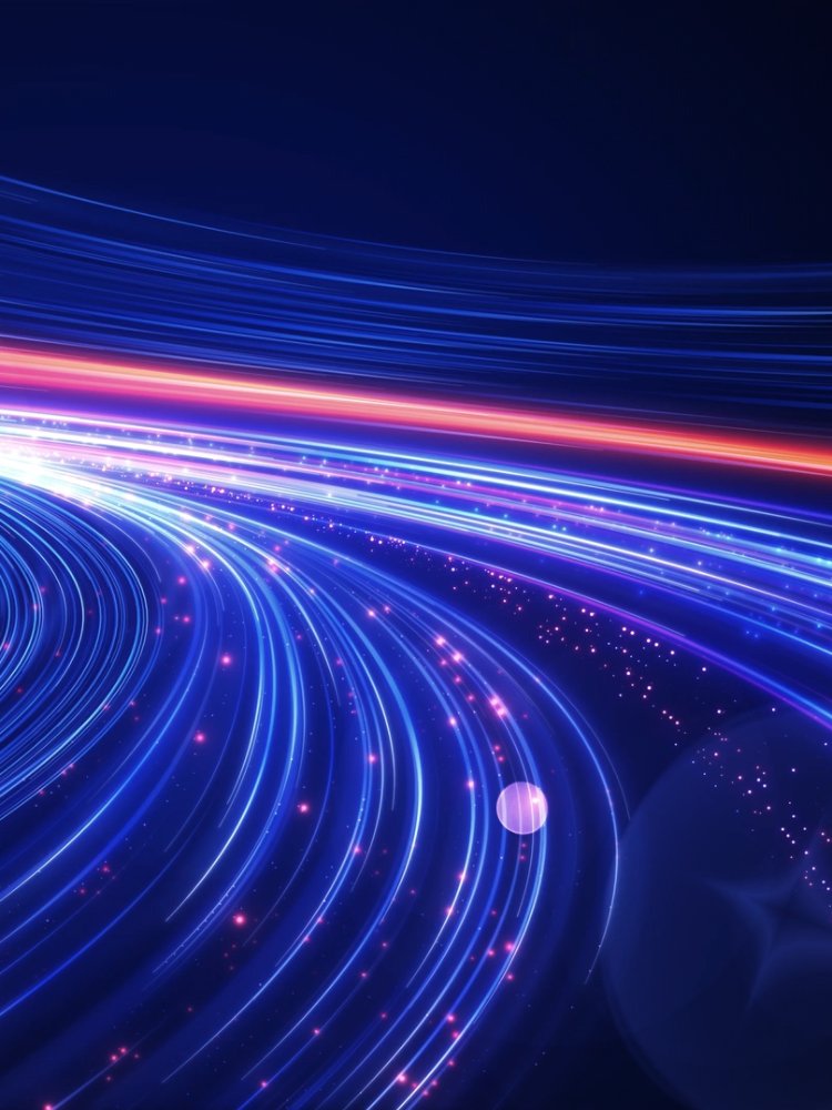 Abstract blue and red light trails curve across a dark background, suggesting high-speed motion and digital connectivity. The scene resembles a futuristic highway or data stream with glowing particles scattered along the paths. Bright neon lines create a sense of depth and perspective, converging toward the distance. Overall, the image conveys technology, speed, and modern innovation.