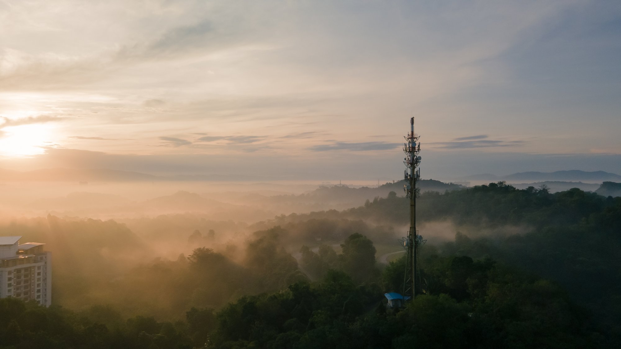 Aerial view of Communication tower during morning sunrise with clouds, mists and fog