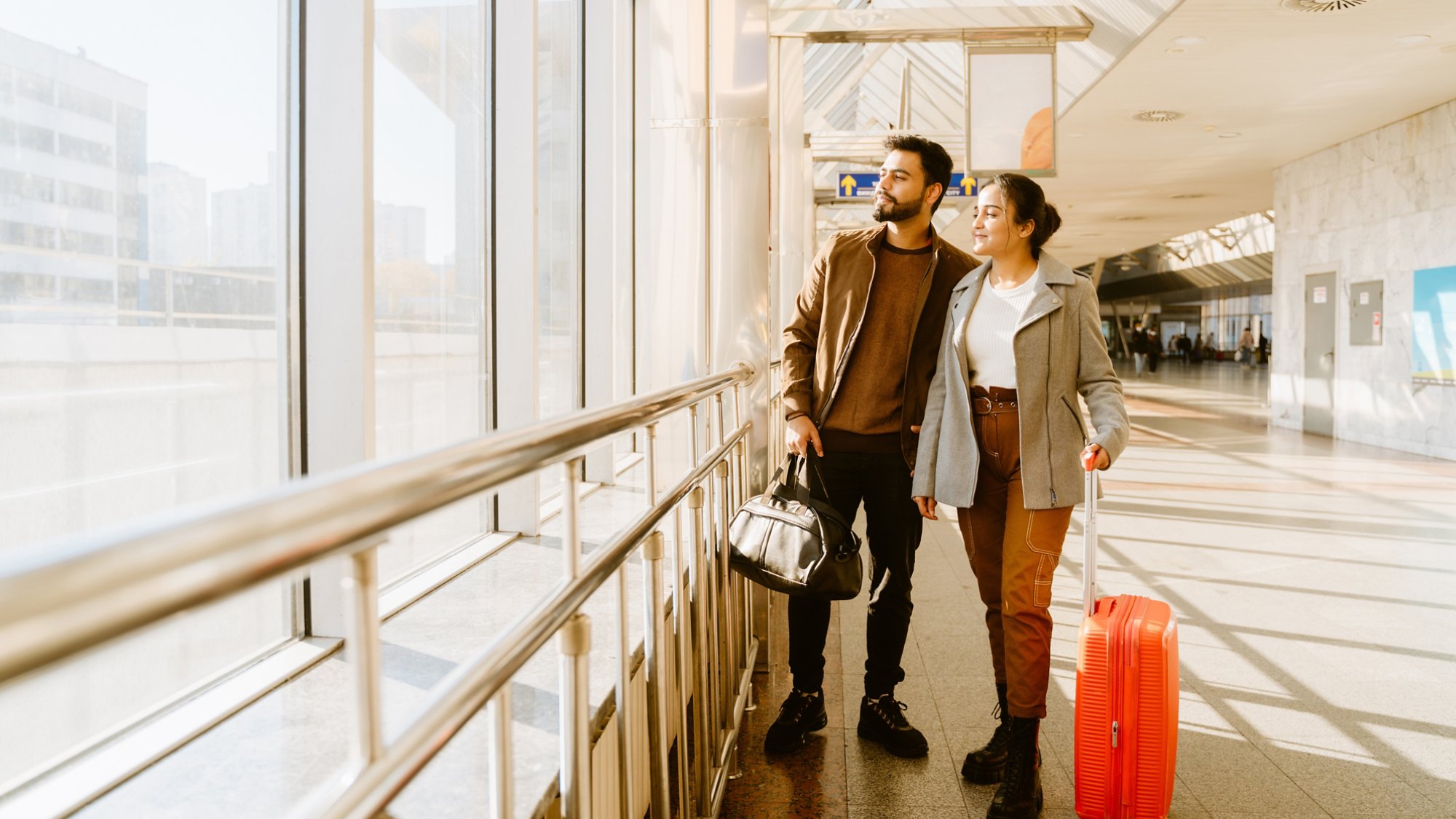 Young indian couple looking in window together at airport indoors