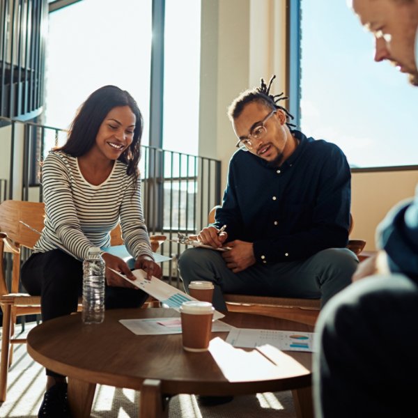 Two smiling young African American businesspeople discussing paperwork with colleagues during a meeting in the lounge of a modern office