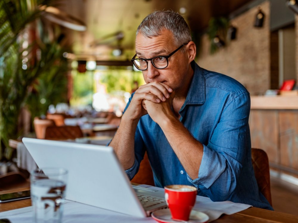 Contemplating businessman in the restaurant feeling sad. Full concentration on work. Confident mature man working on laptop while sitting at his working place in office. Tired manager sitting in restaurant surrounded with coffee and laptop computer having tired look , having pain, being sleepy and exhausted. Tiredness.